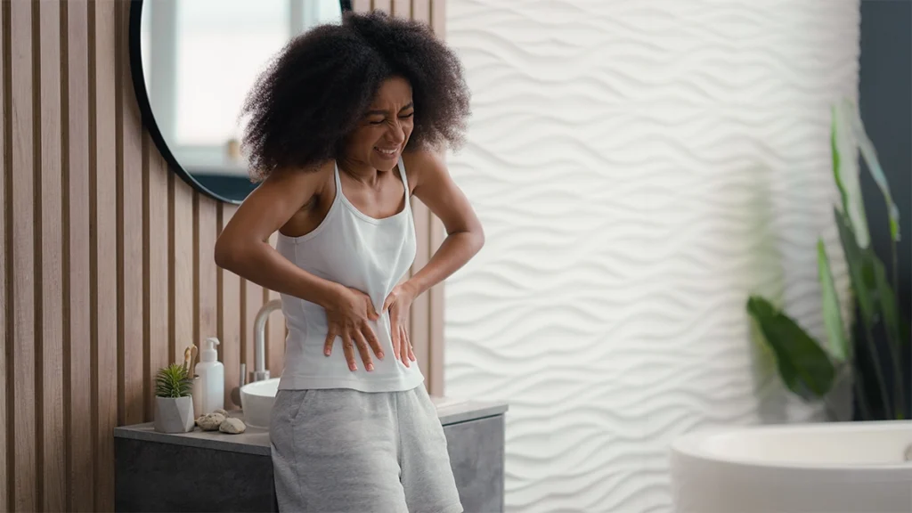African woman holding stomach in pain in bathroom